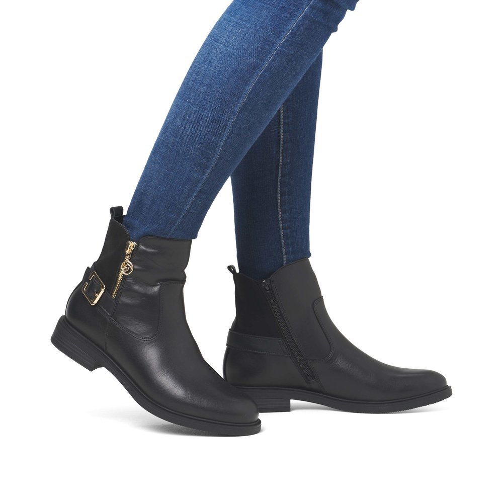 Night black remonte women´s ankle boots D1U71-00 with a golden decorative buckle. Shoe on foot.