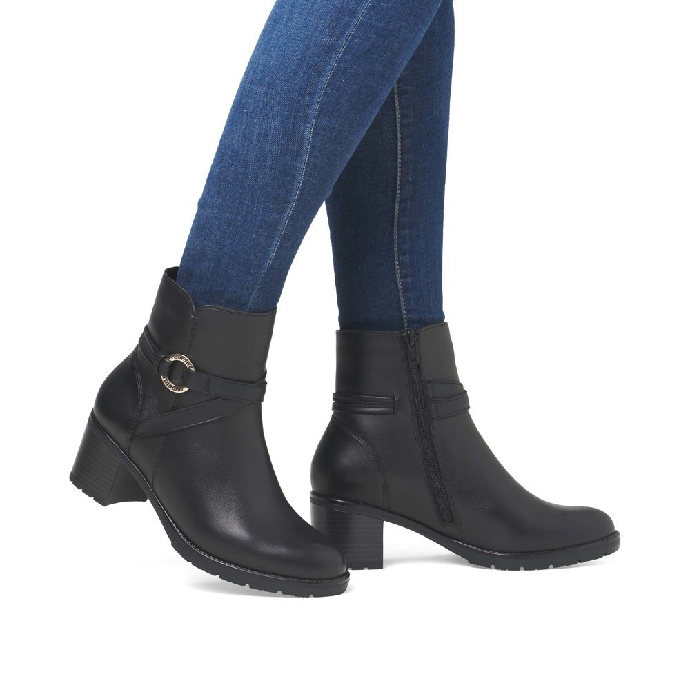 Jet black remonte women´s ankle boots D2A73-00 with a round decorative buckle. Shoe on foot.