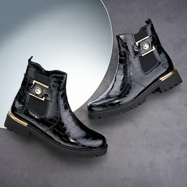 Lackschwarze remonte Chelsea Boots D8684-03 mit goldenem Schmuckelement. Schuhe auf dunklem Hintergrund.