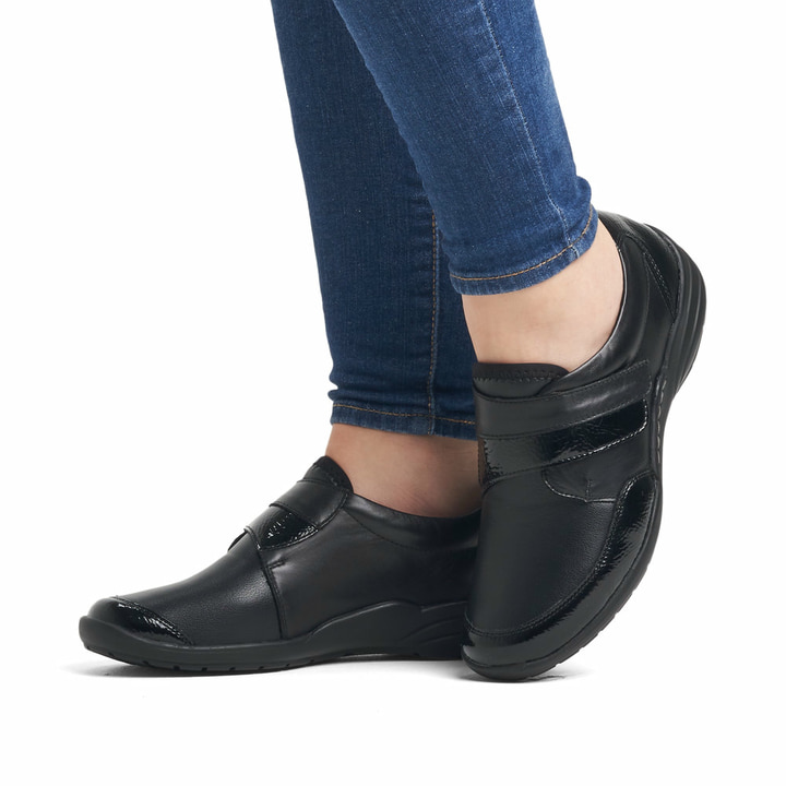 Schwarze remonte Damen Slipper R7600-04 mit Klettverschluss sowie Extraweite H. Schuh am Fuß.