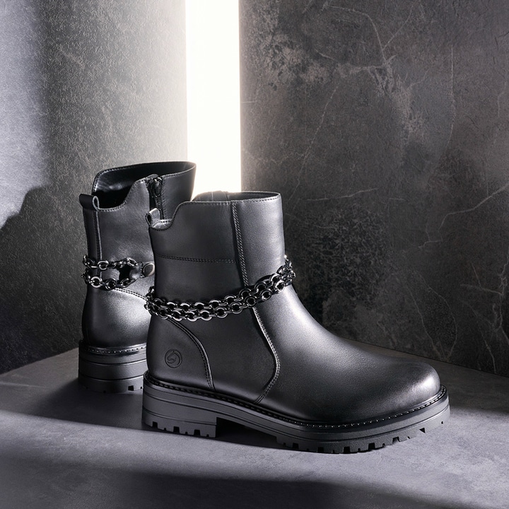 Nachtschwarze remonte Damen Kurzstiefel D2285-00 mit abnehmbarer Kette. Schuhe auf dunklem Hintergrund.