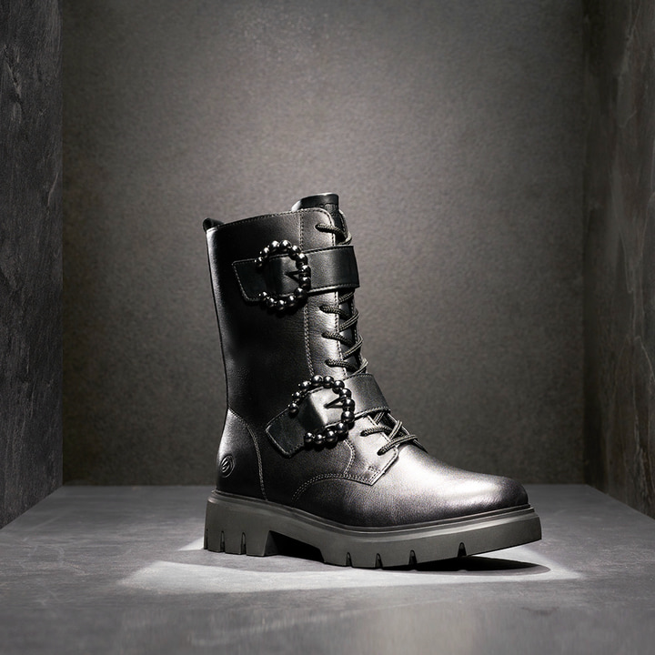 Tiefschwarze remonte Damen Biker Boots D1W70-00 mit runden Zierschnallen. Schuh auf dunklem Hintergrund.